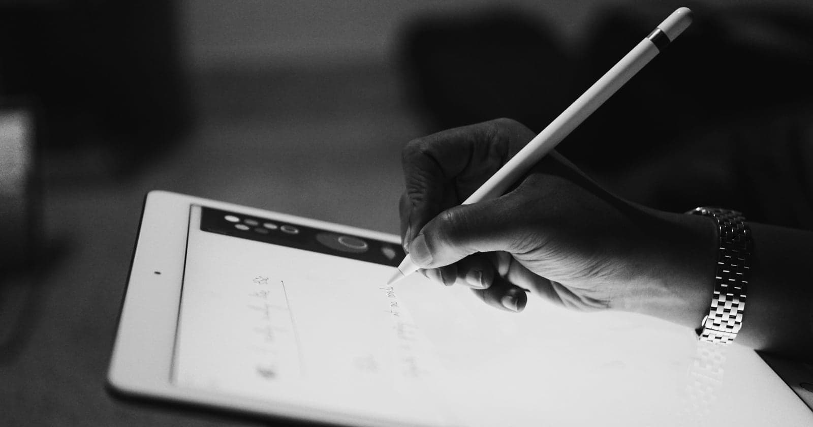 A hand writes on a tablet screen with a stylus.