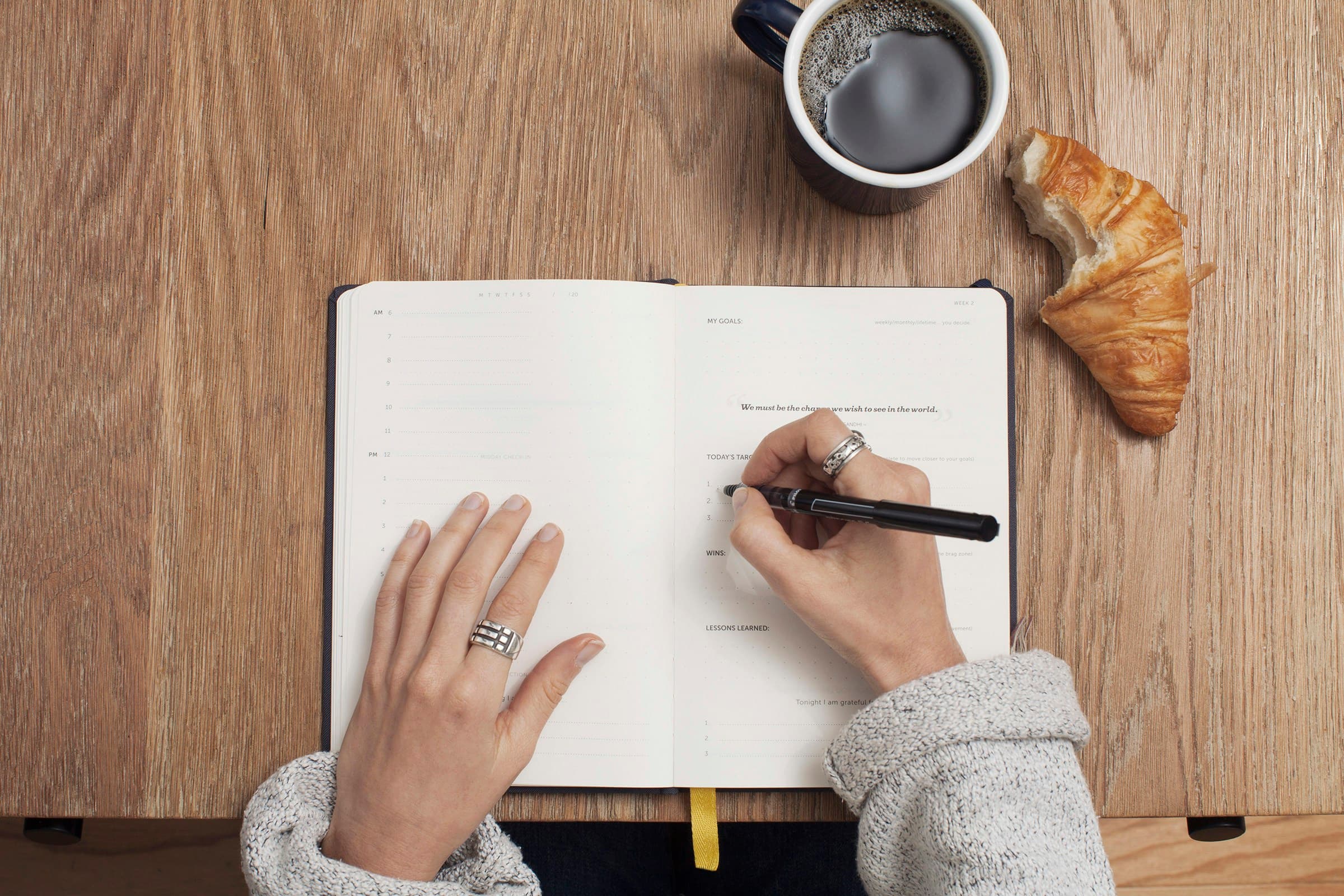 A person writes in a journal with a pen beside a cup of coffee.