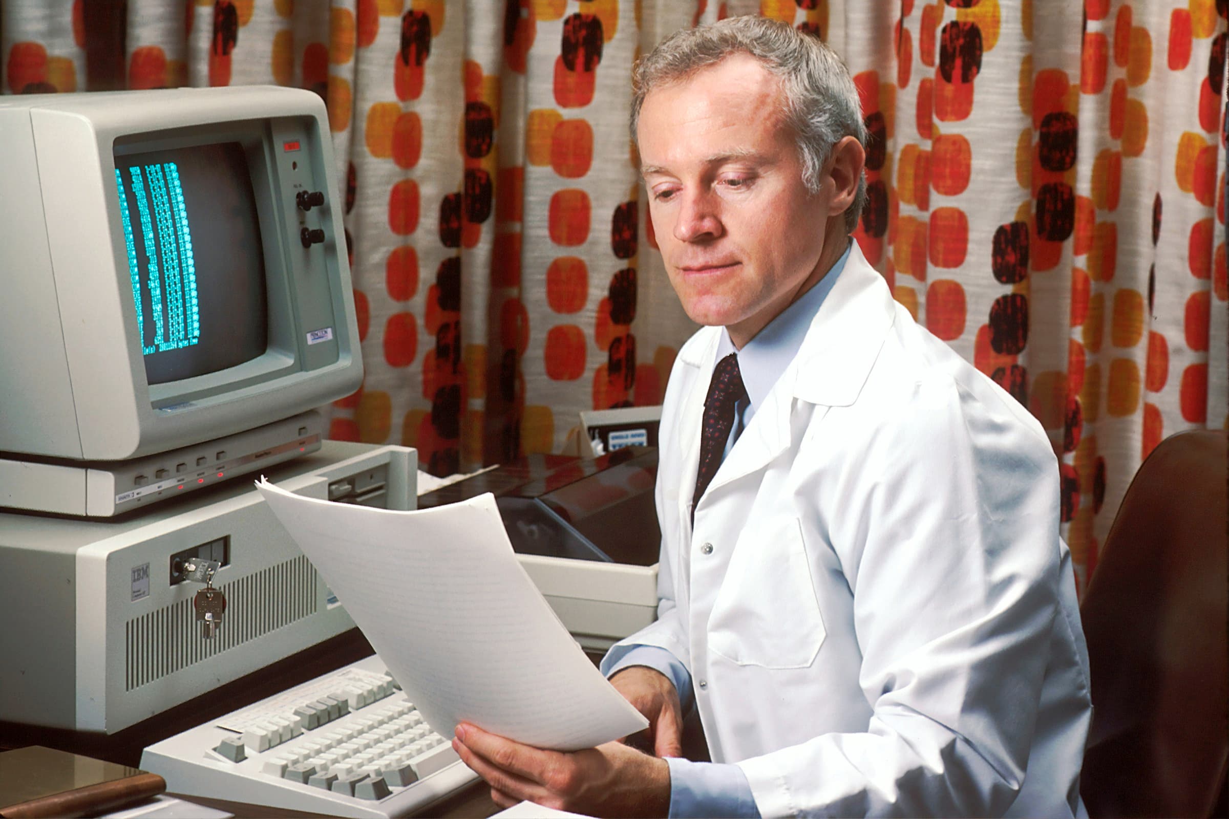 A physician reviews a printed medical reference beside a computer.