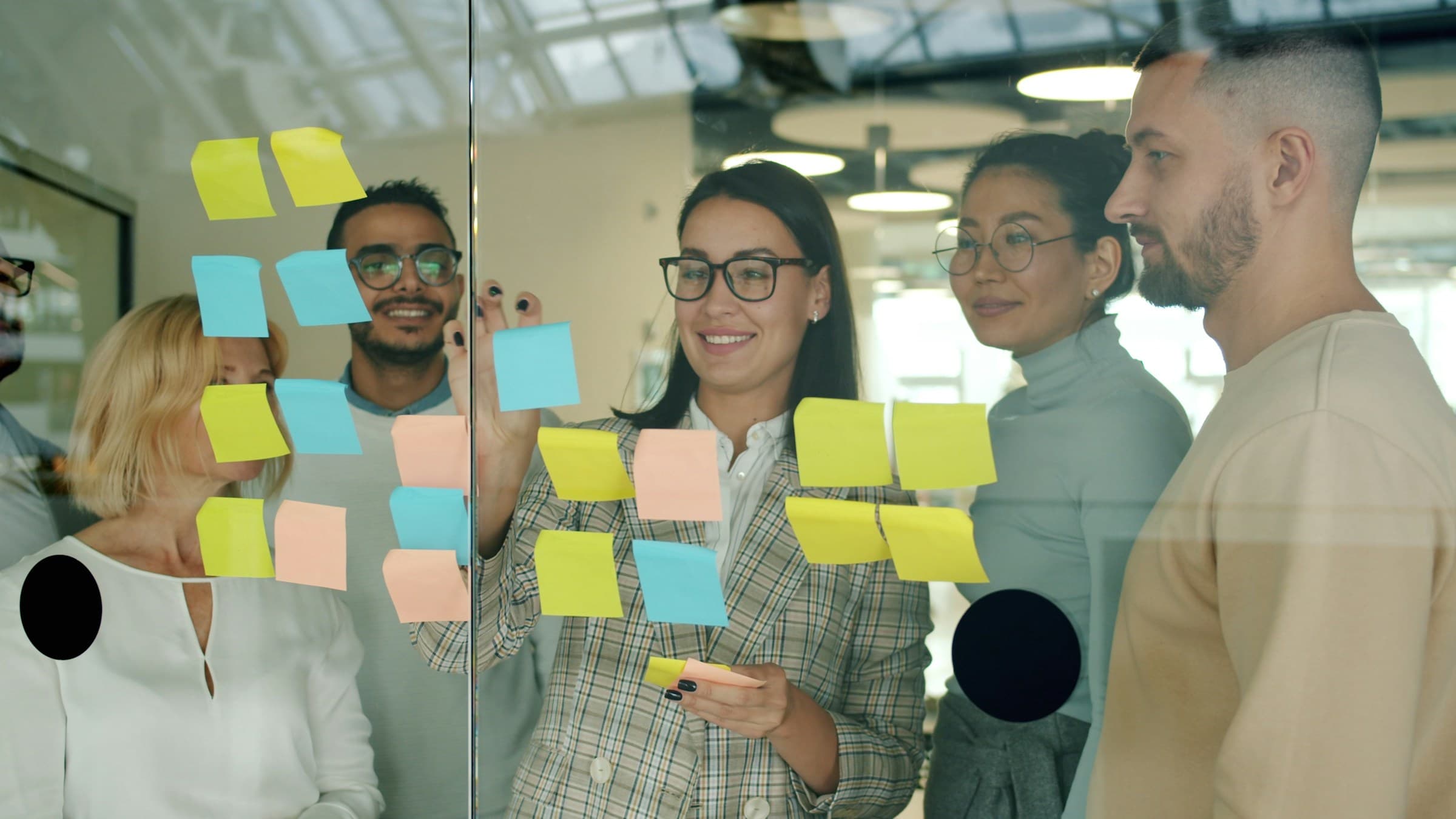 Research team members arranging sticky notes on a glass wall during an affinity mapping session.