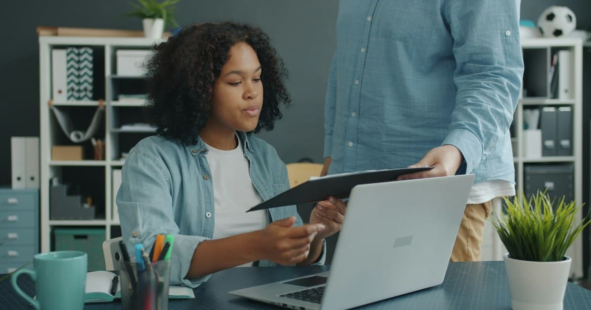 Two colleagues review documents together at a laptop.