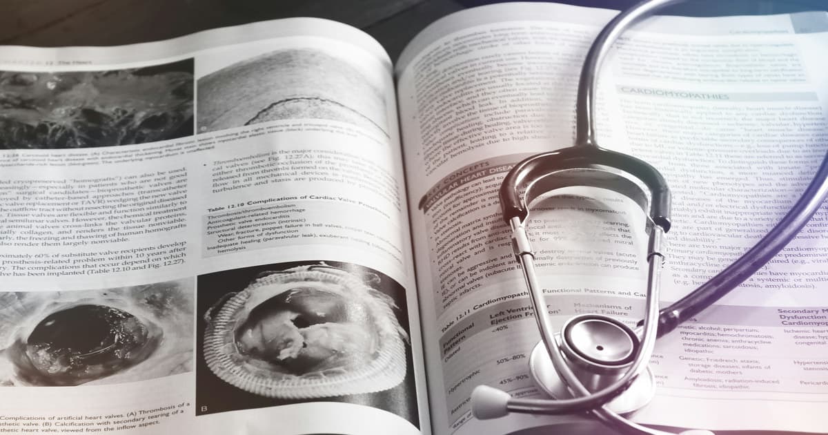 An open medical textbook with cardiac diagrams and a stethoscope resting across its pages.
