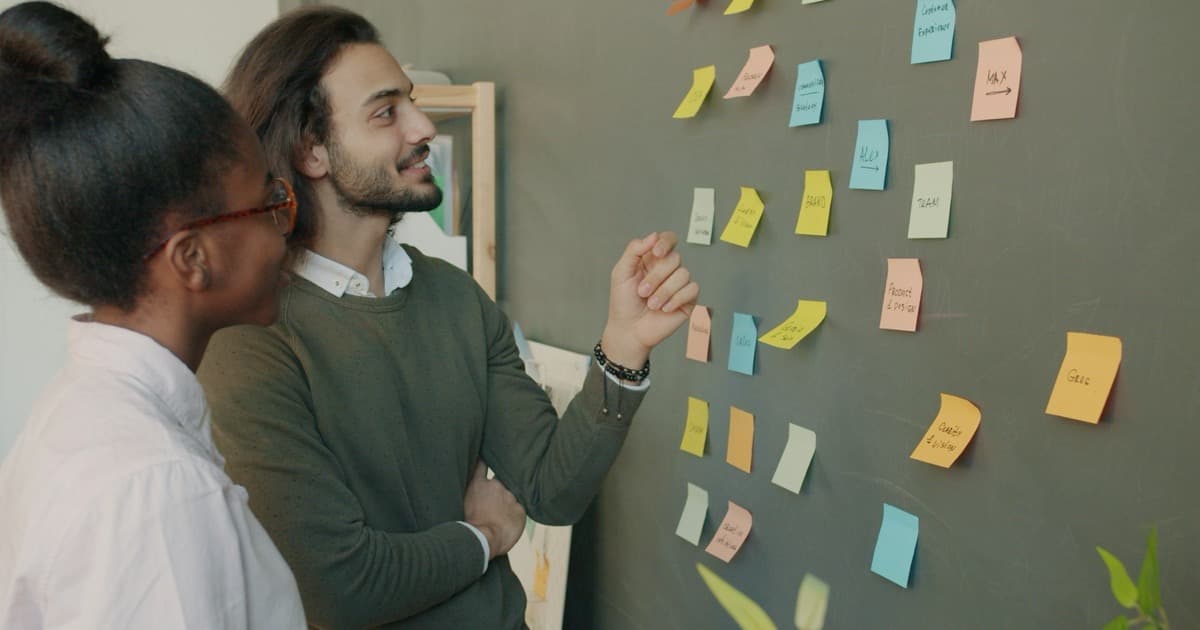 Two colleagues discuss sticky notes on a wall during a workshop.