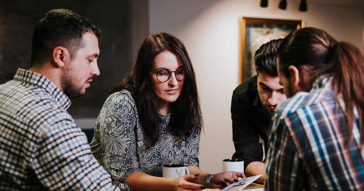 Four people review printed pages at a table.