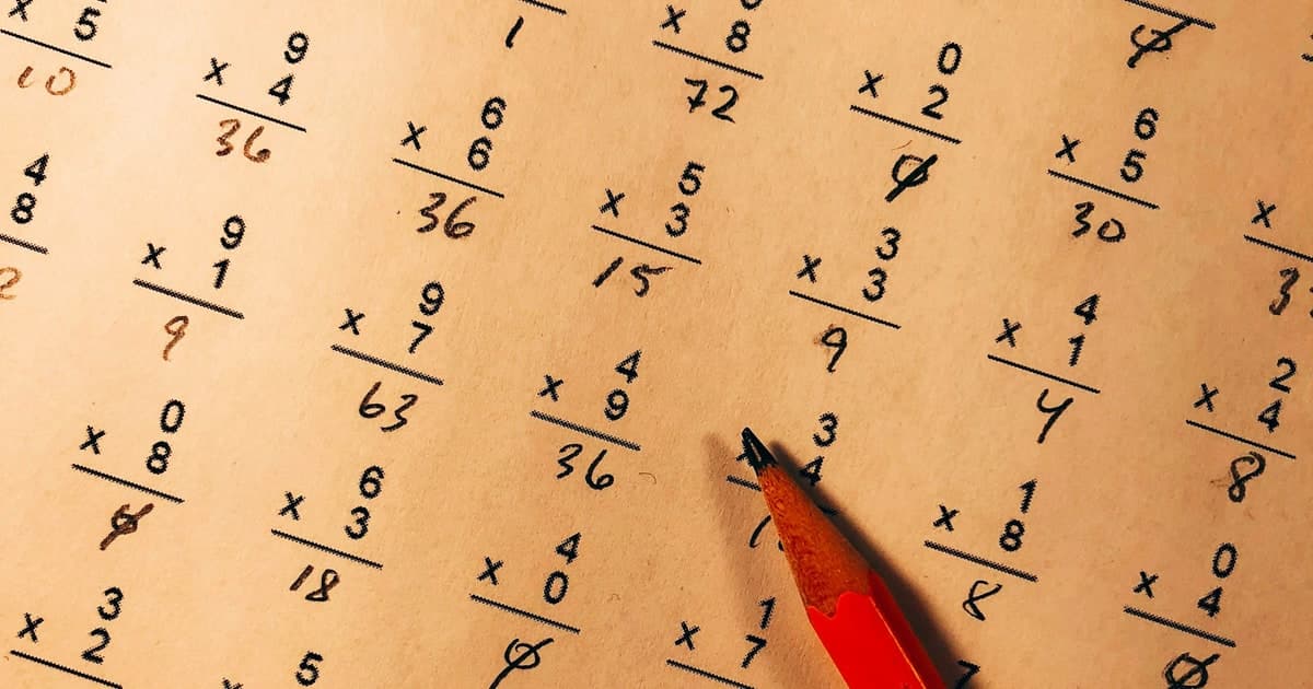 A red pencil points to worked arithmetic problems on a quiz sheet.