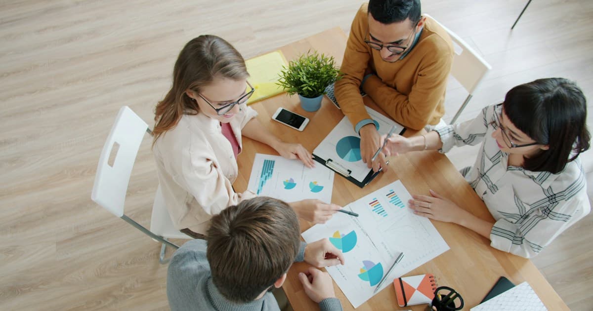 Colleagues compare printed charts around a table.
