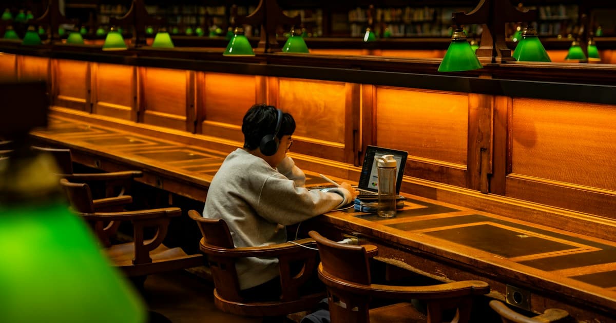 A person studies on a laptop at a long wooden desk in State Library Victoria.