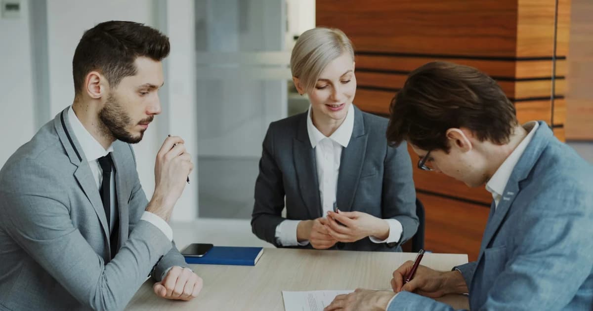 Three professionals review and sign paperwork at a table.