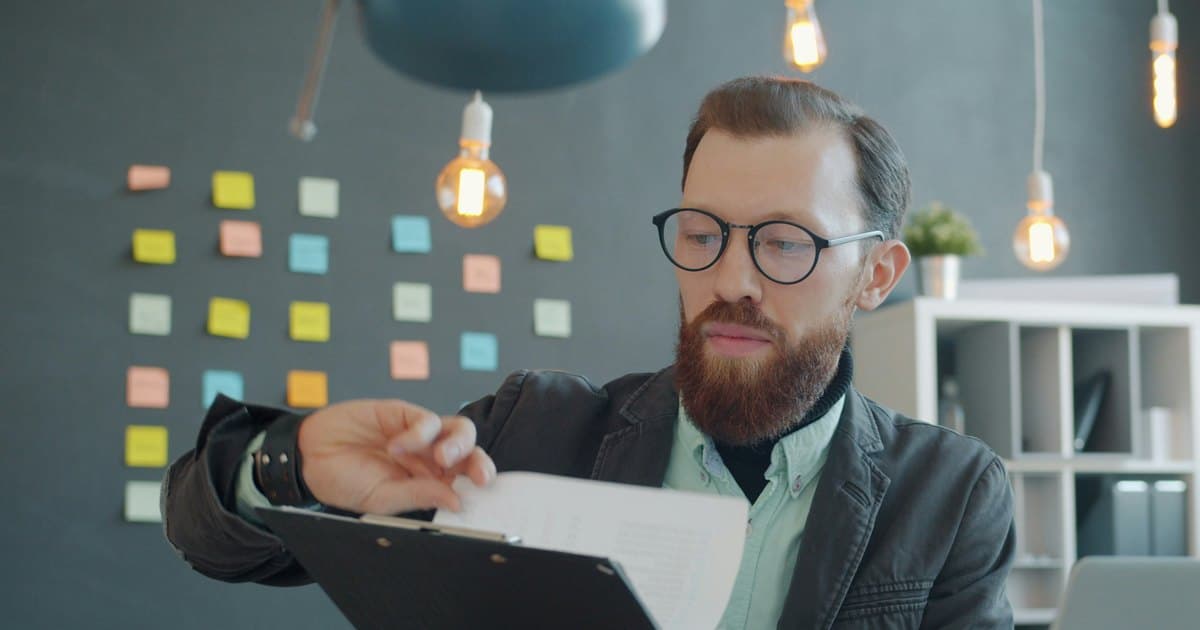 A man reads a printed document on a clipboard.