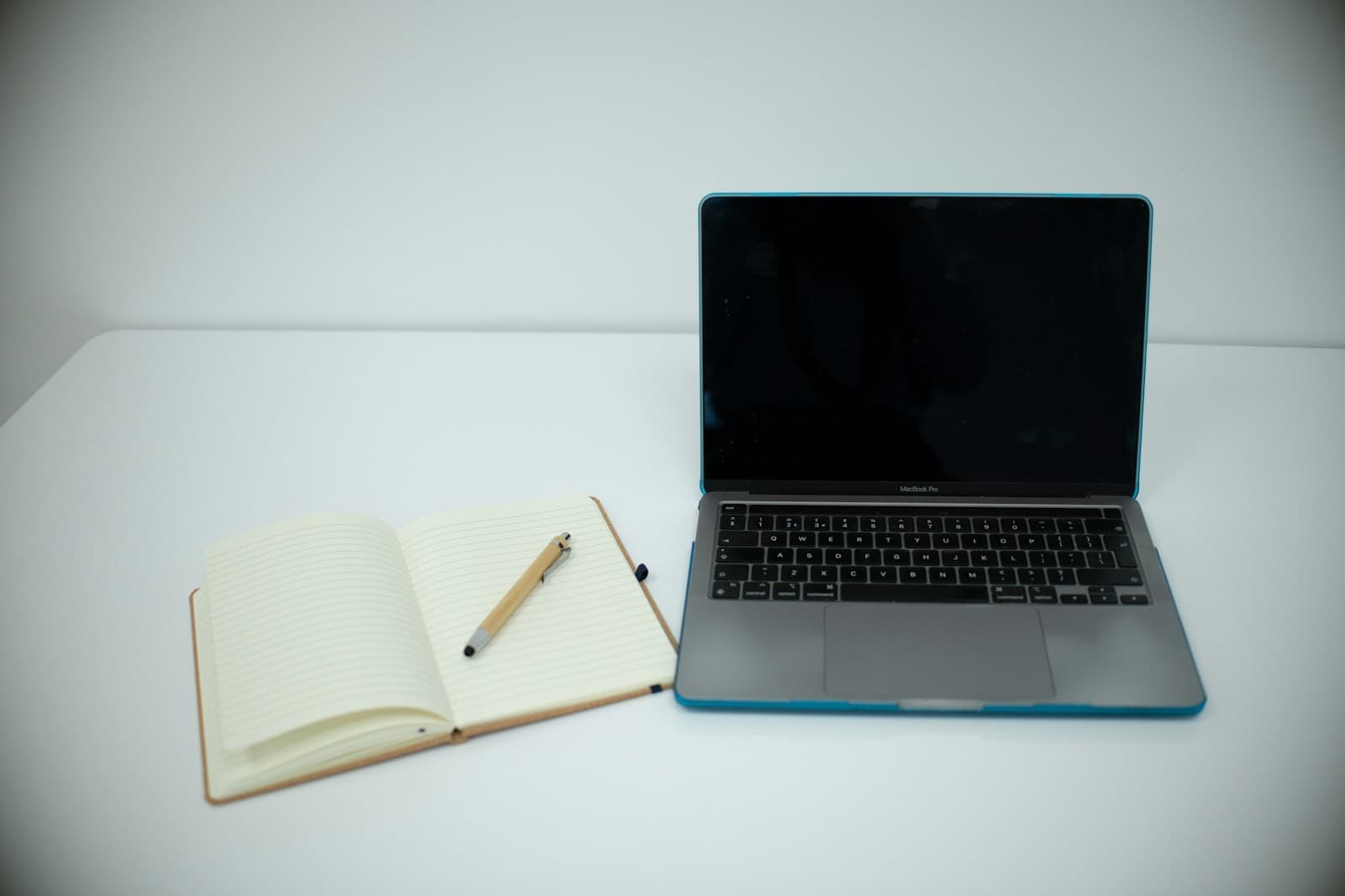 An open notebook sits beside a laptop and pen.