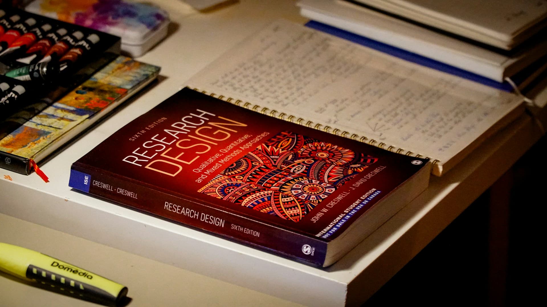 A research-design book sits beside marked notes, notebooks, and study materials.