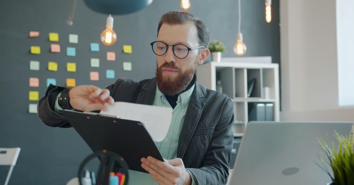 An office worker checks a printed page beside a laptop.