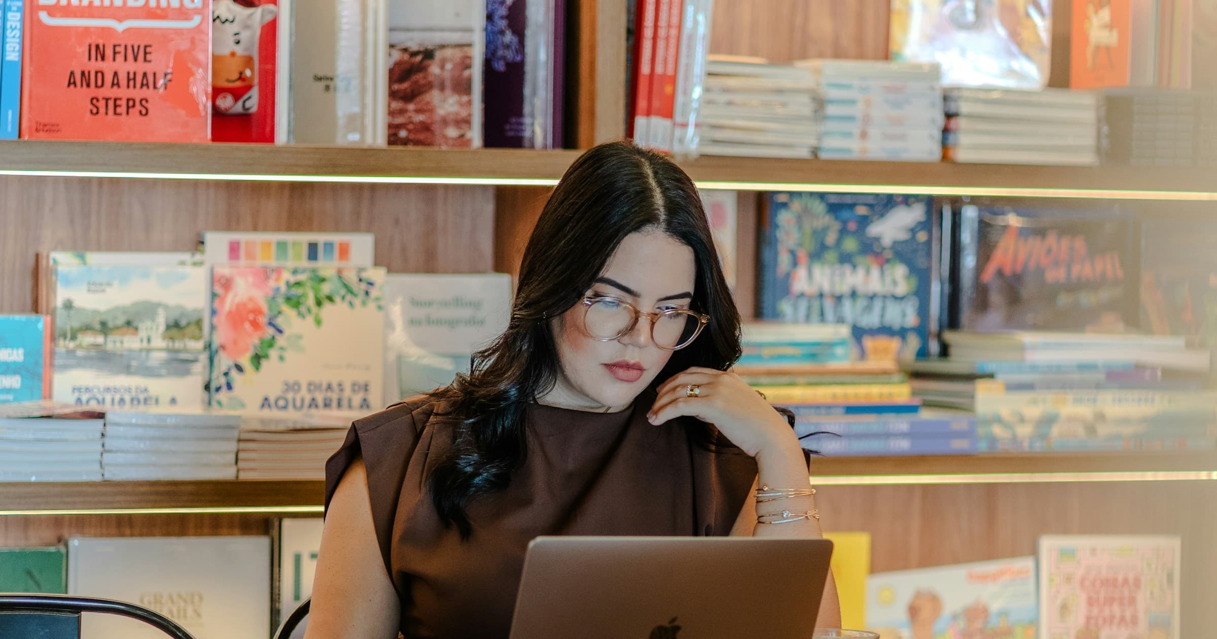 A woman works on a laptop among displays of books.