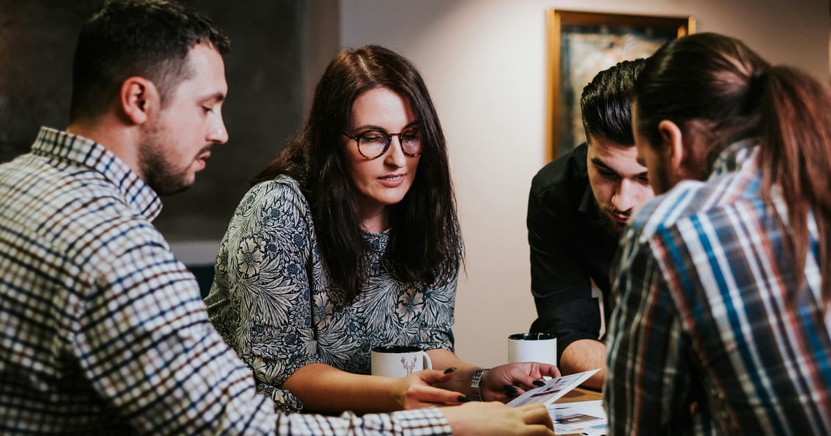 Four people review printed pages together.