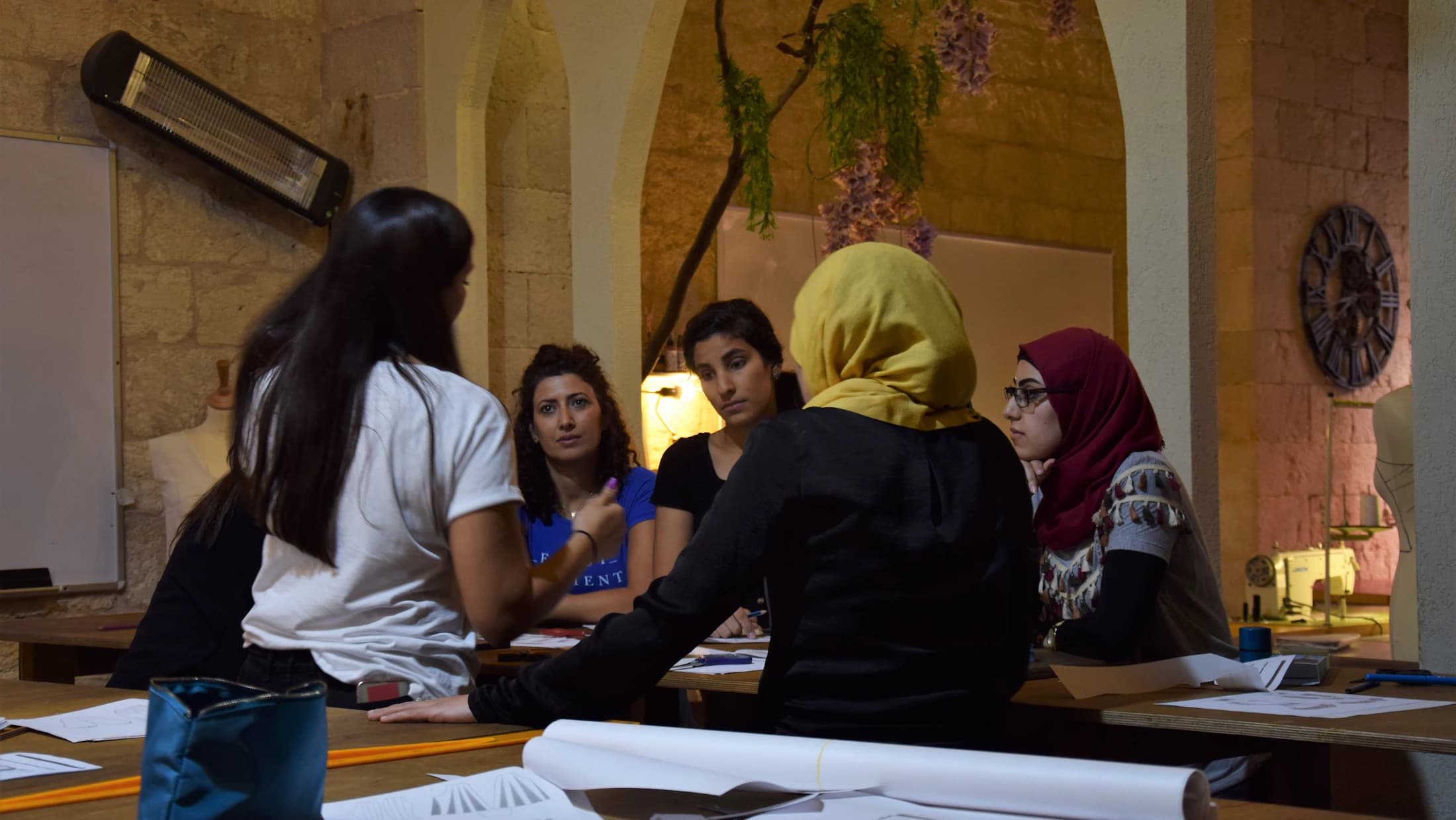 A facilitator and participants discuss a topic around a table with papers in front of them.