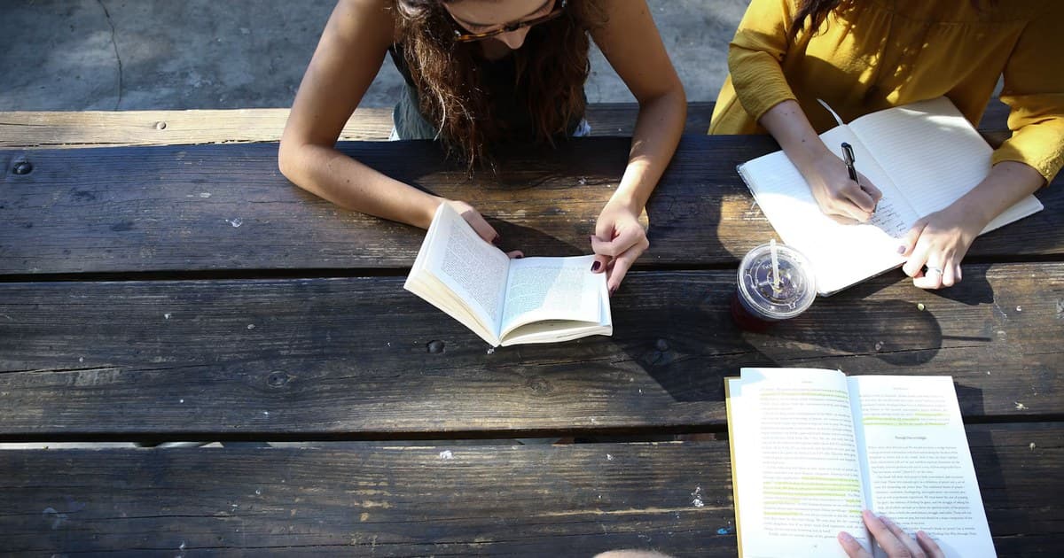 People read open books while one person writes notes in a notebook.