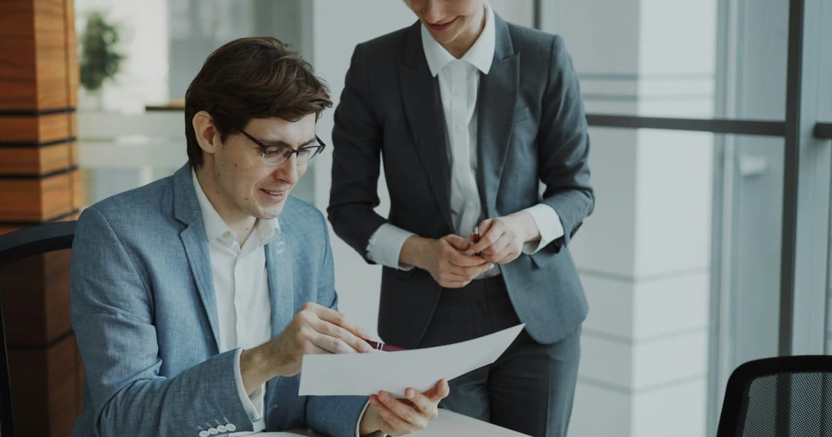 Two colleagues review a printed document together at a desk.