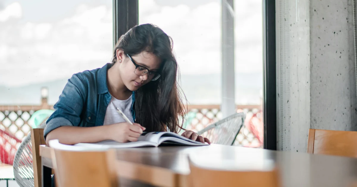 A person writes in an open book at a table.