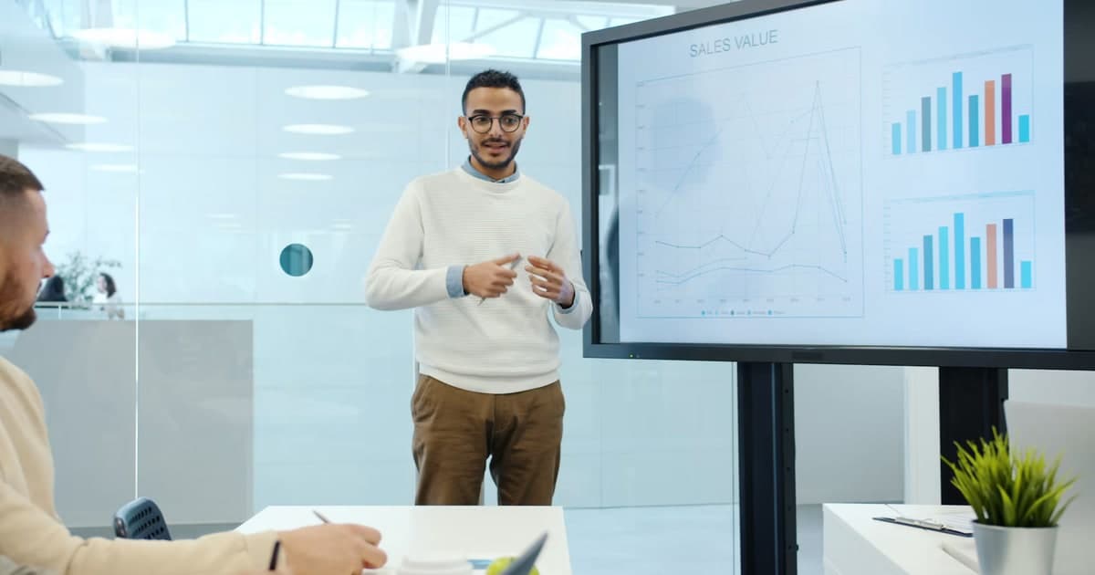 A presenter discusses charts on a screen during a meeting.