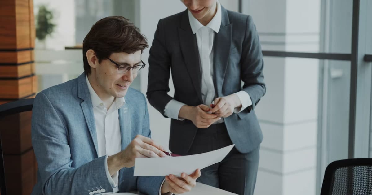 Two colleagues review a printed document together at a desk.