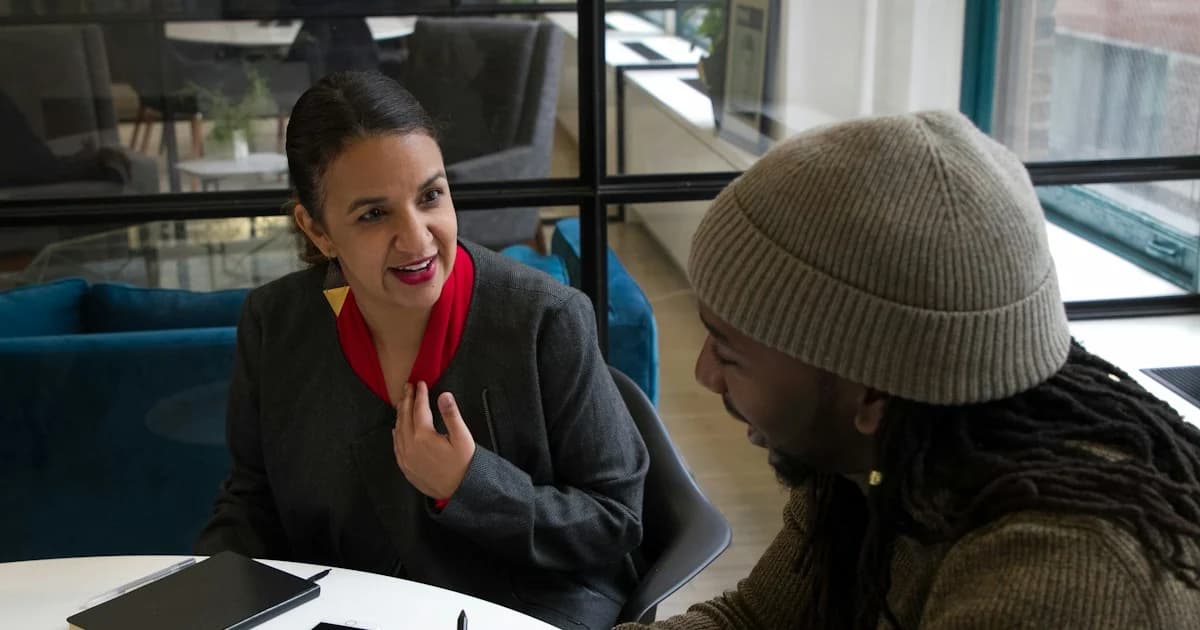 Two people talk across a table during a meeting.
