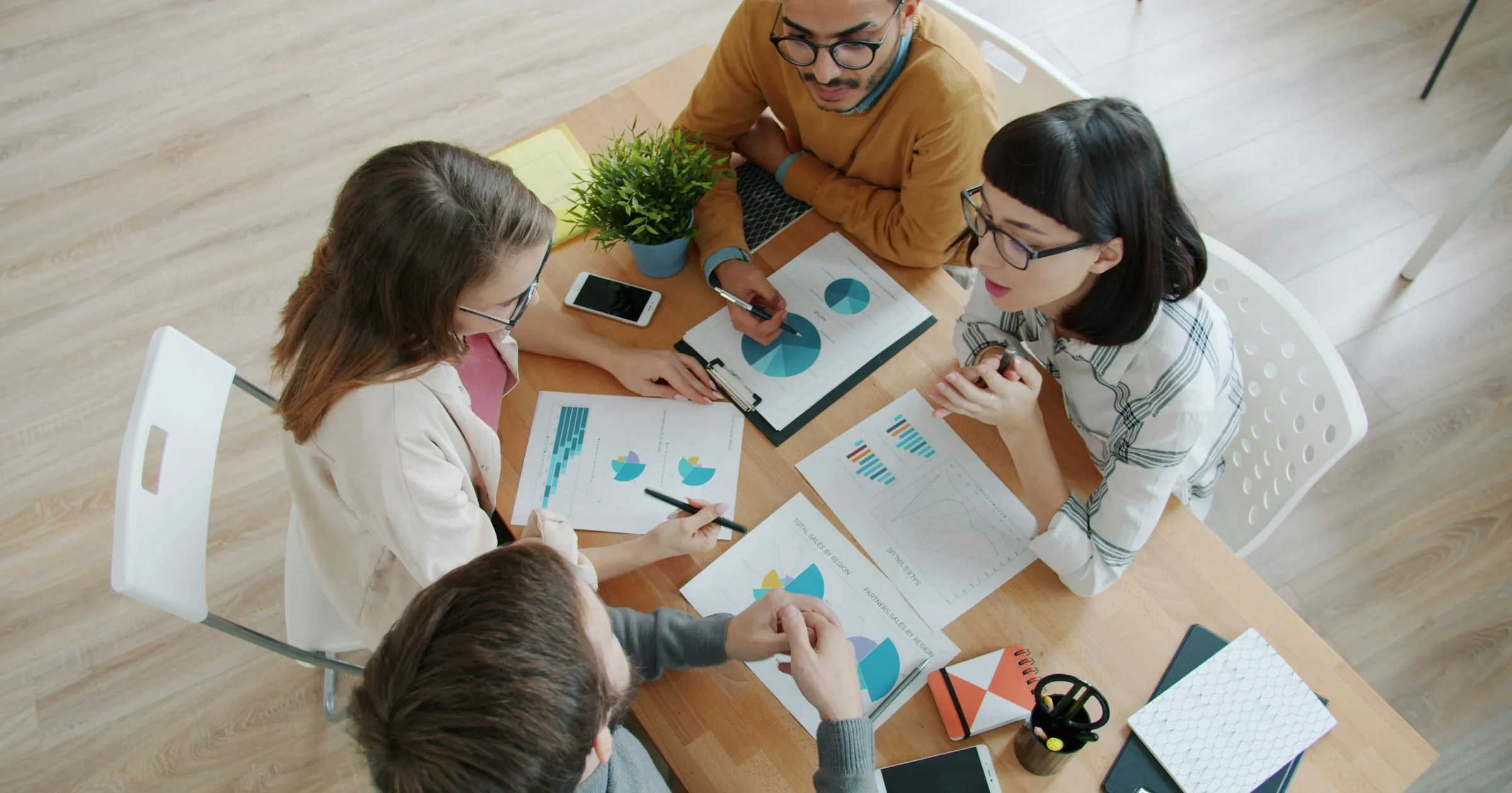 Four colleagues review printed charts and notes around a table.
