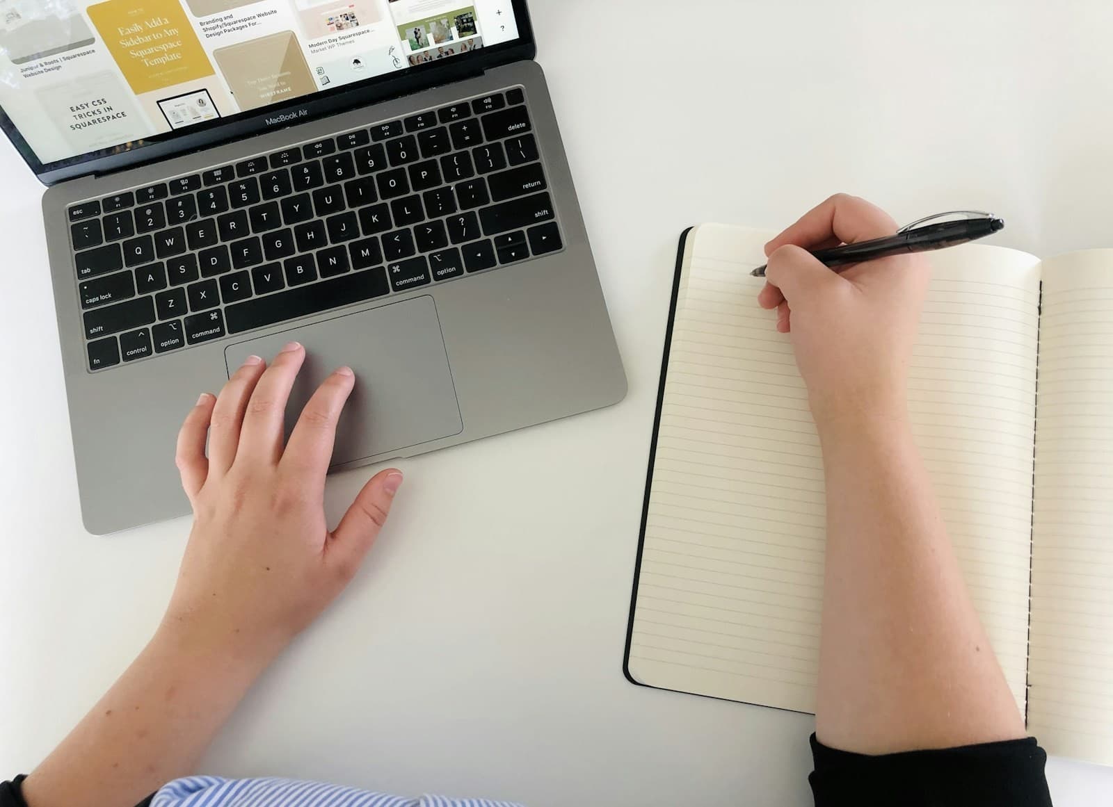 A person writes in a notebook beside a laptop.