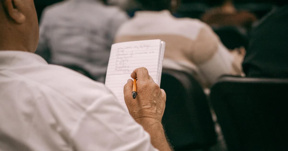 A person writes in a notebook during a meeting.