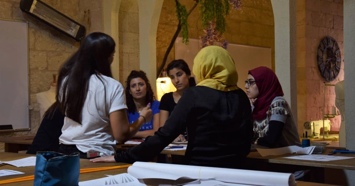 A facilitator and several participants discuss a topic around a table with papers.