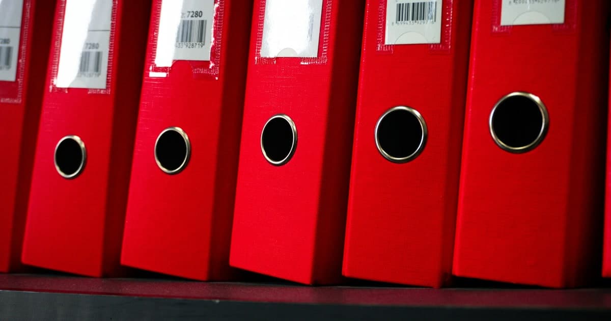 Red file binders with barcode labels line an office shelf.
