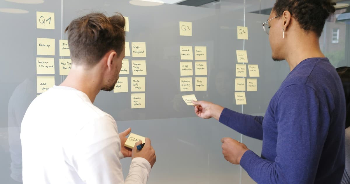 Two colleagues organize sticky notes on a quarterly planning board.