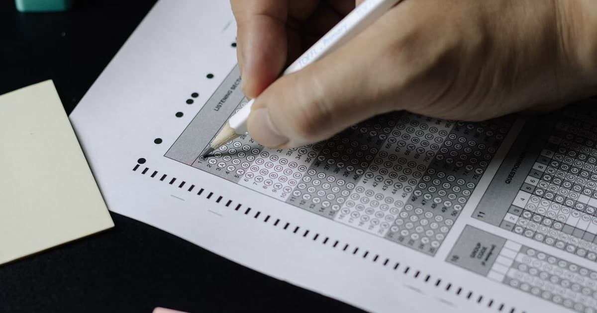 A hand fills in bubbles on a printed multiple-choice exam answer sheet.