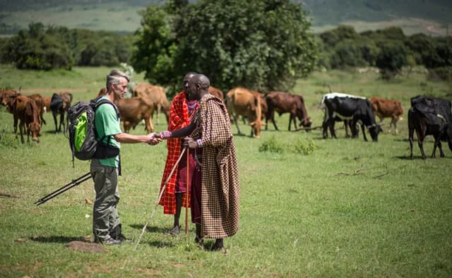 Josphat Mako greets Stuart Butler near grazing cattle, photographed by Stuart Price for Make It Kenya, public domain