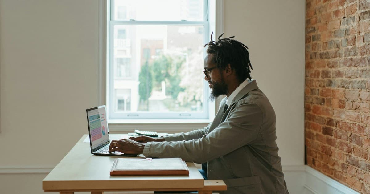 A person researches at a laptop with papers on the desk.