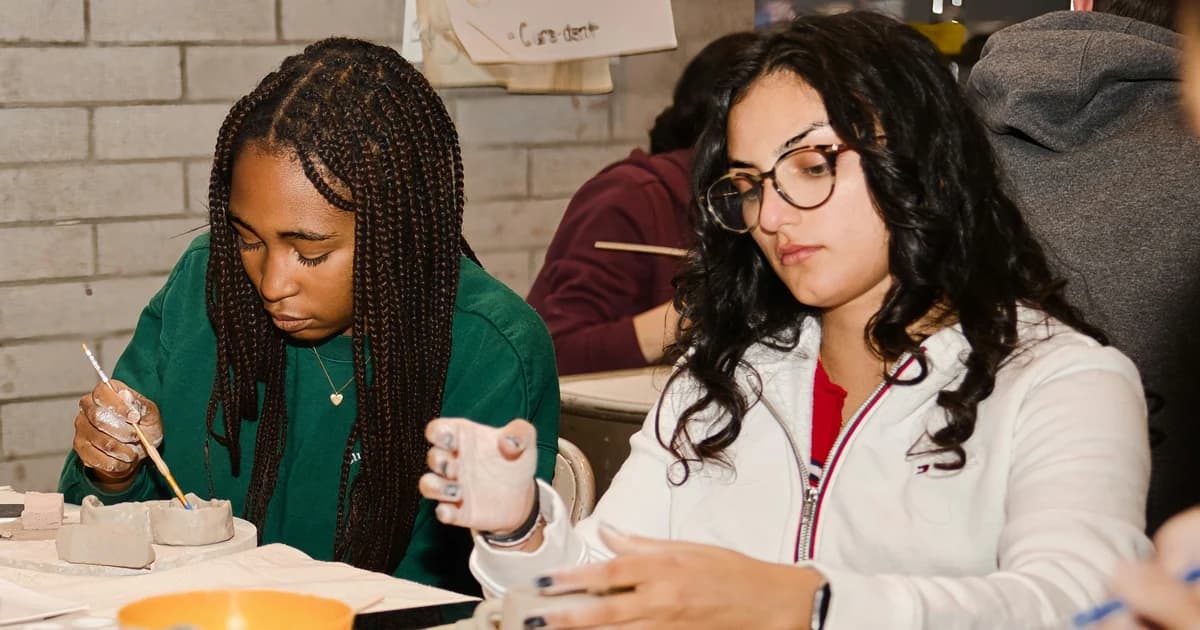 Two people shape clay at a table during a class activity.