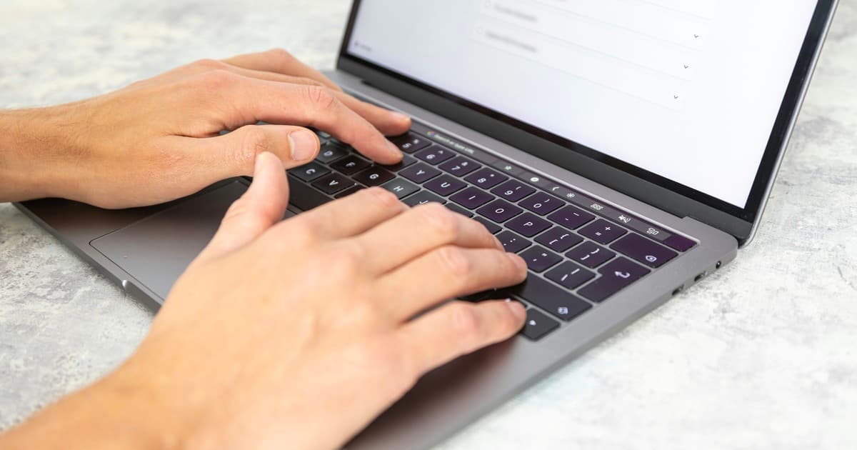Hands type on a laptop.