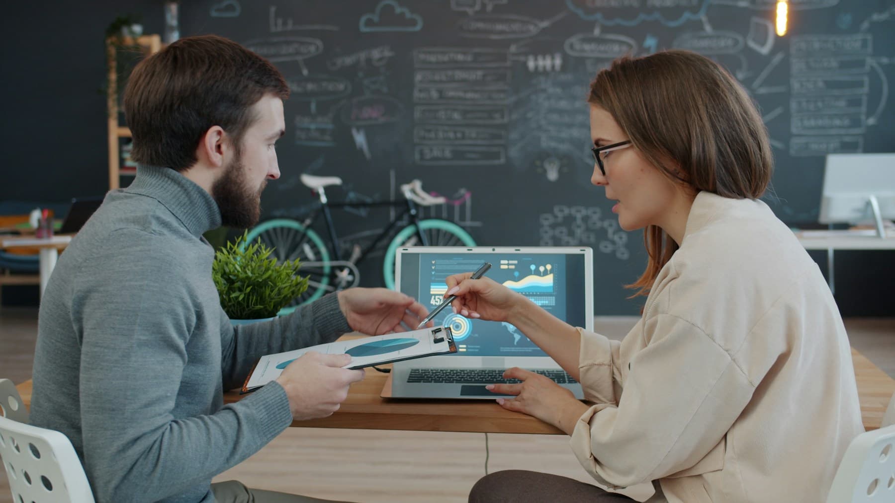 Two colleagues review a chart on a laptop together.