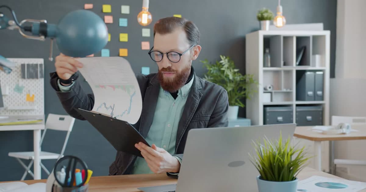 A person reviews printed charts beside a laptop at a desk.