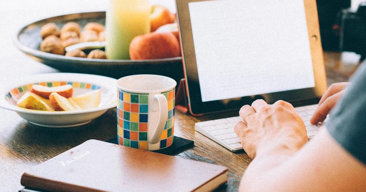 A person works with a tablet and laptop at a desk.
