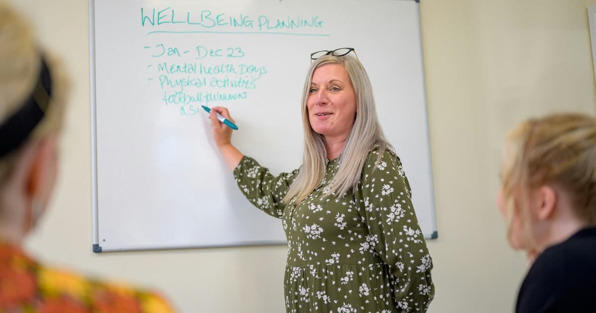 A woman outlines a wellbeing plan on a whiteboard during a meeting.
