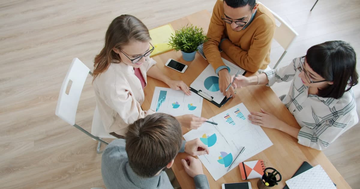 Four colleagues discuss printed charts around a table.