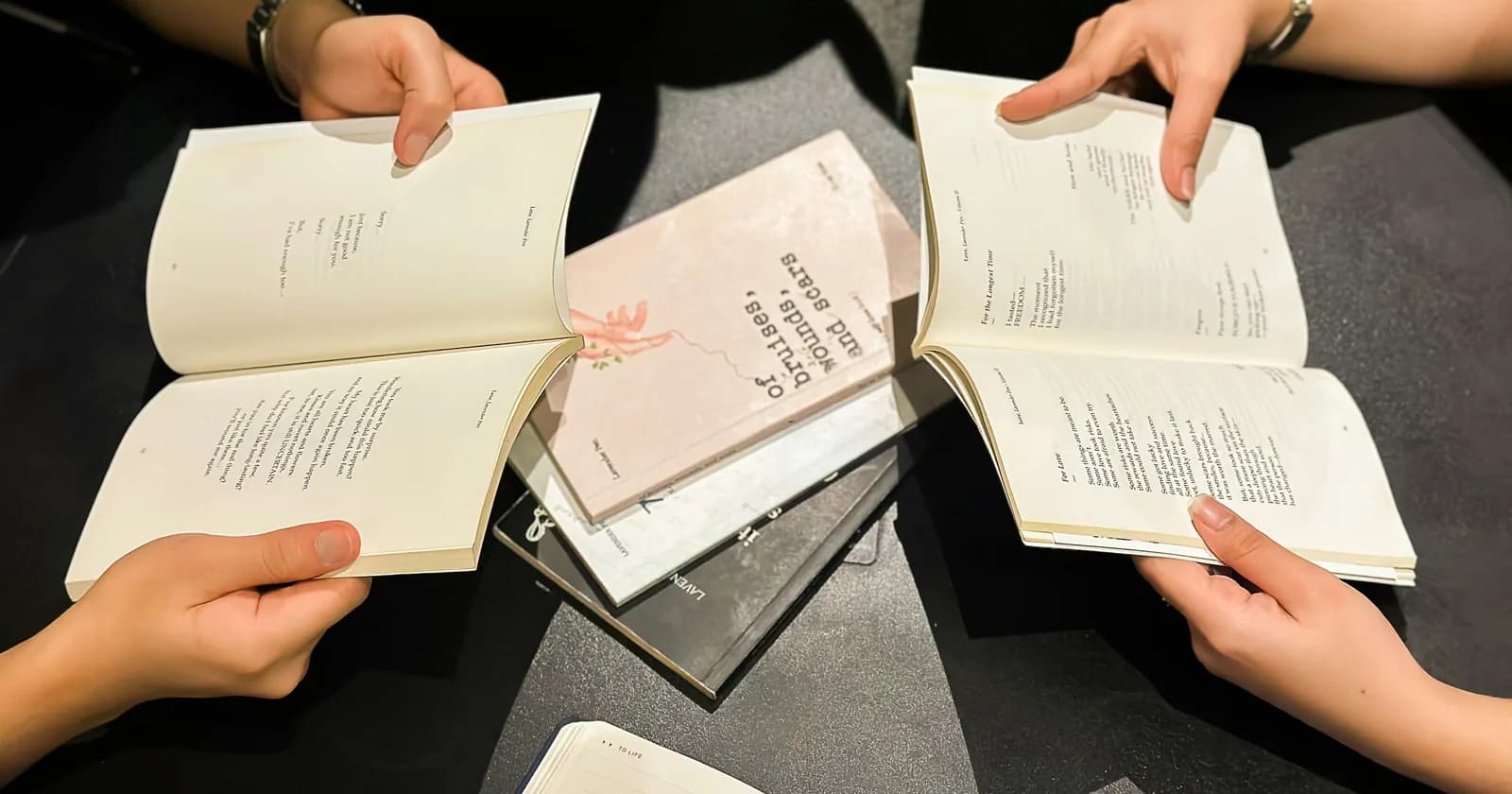 Readers hold several open books around a shared table.