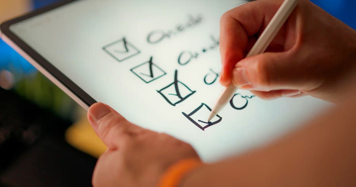 A hand checks boxes on a tablet with a stylus.