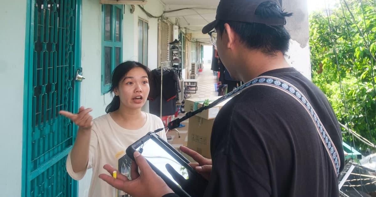 A woman talks with a man holding a tablet outdoors.
