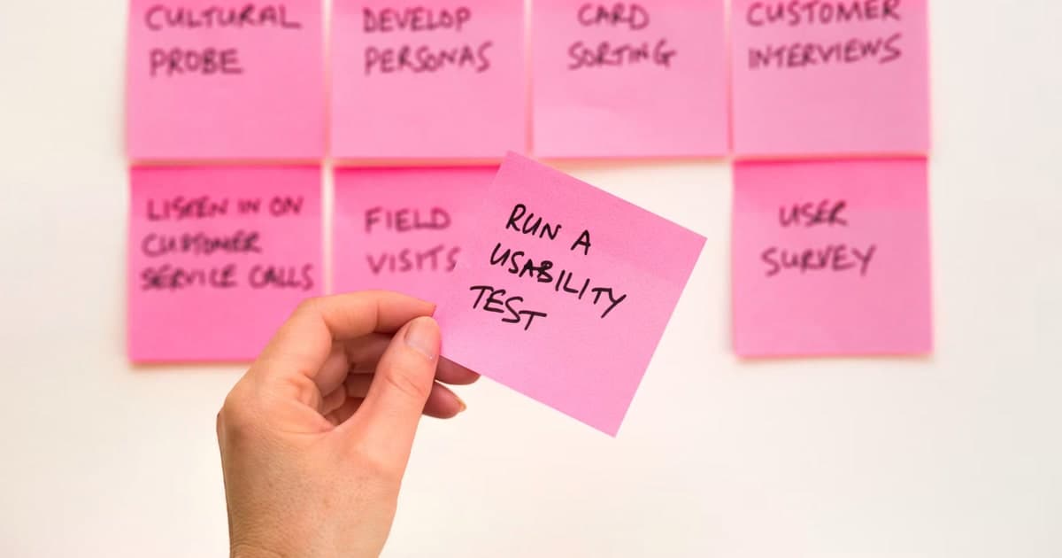 A hand holds a pink note that reads “Run a Usability Test.”