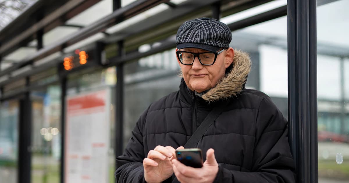 A person uses a phone while waiting at a transit stop.